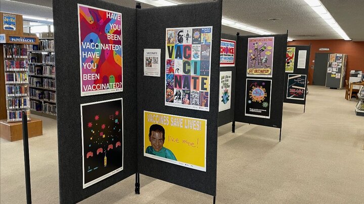 A row of dark grey panels with colorful posters on them displayed in a library