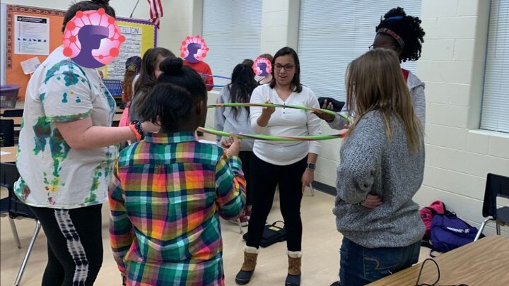 College student mentors and middle school youth in an after school club work together to hold a hula hoop level usng only one finger per person