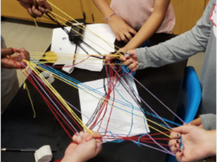 Hands holding a network model made of different colored yarn.