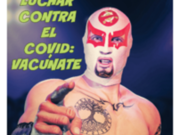 In stadium, tattooed masked wrestler points at viewer. Their mask is white and red around the eyes and on the forehead is a golden coronavirus with red glyph on it. In bright, light green, bold, capital letters: “Fight COVID: Vaccinate. A luchar contra el covid: vacúnate.”