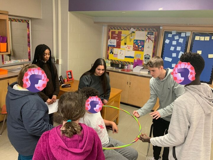 College student mentors and middle school youth in an after school club work together to hold a hula hoop level usng only one finger per person