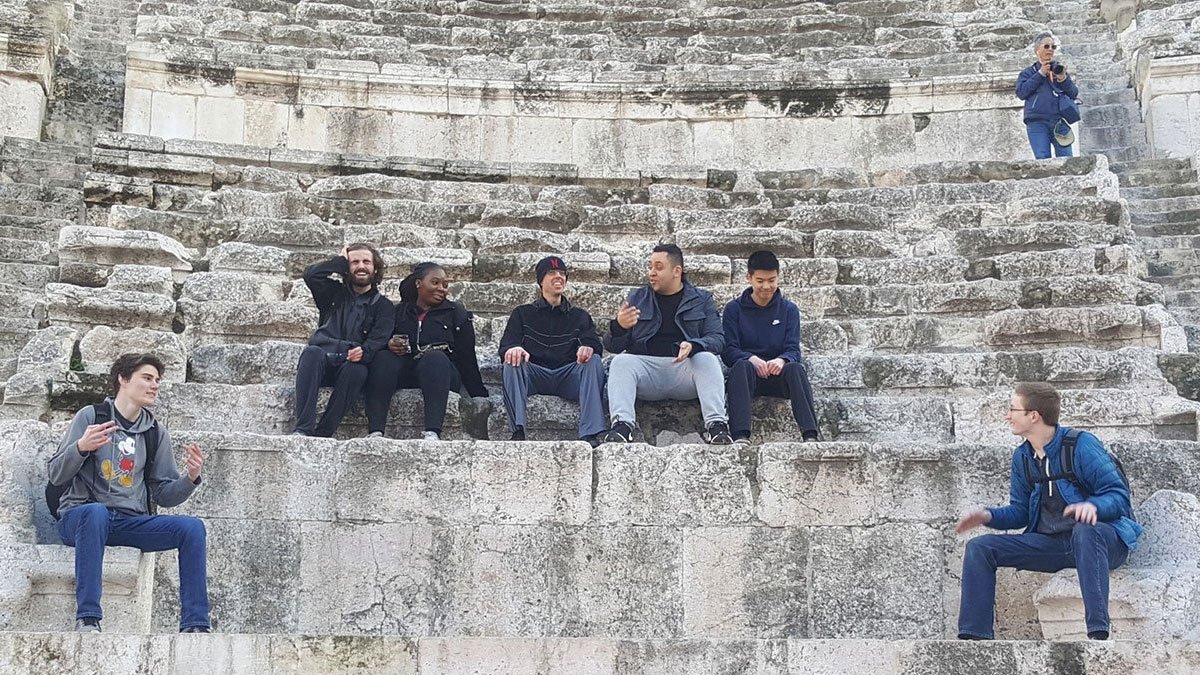 Students studying abroad sitting on ancient stone steps.