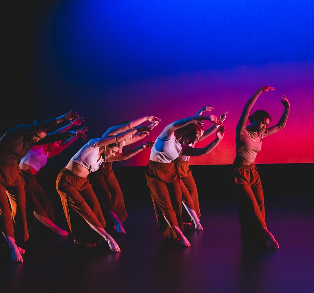 A group of dancers in motion on a darkened stage.