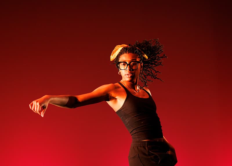 A dancer gestures in front of a dark red background.