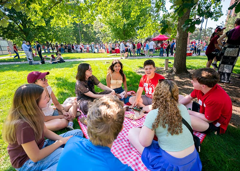 Students sit in a circle talking during a picnic.