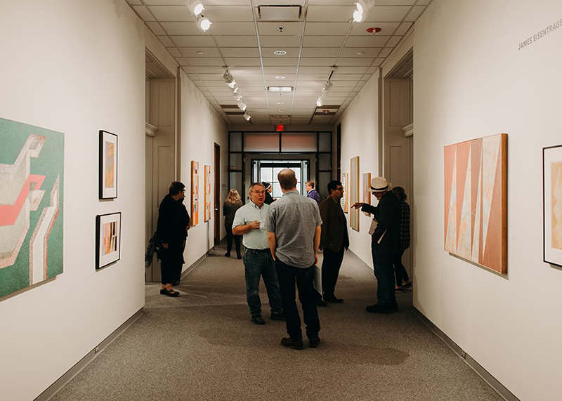 Gallery patrons stand discussing hung paintings.