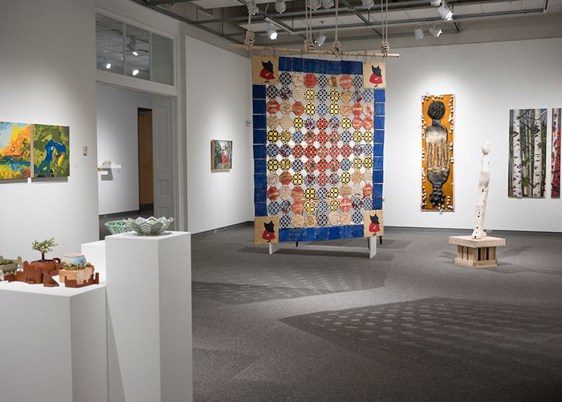 A quilt is hung among the other pieces of art in the gallery.