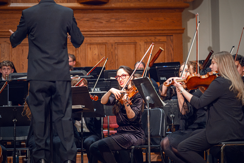 A violinist plays on stage with a symphony.