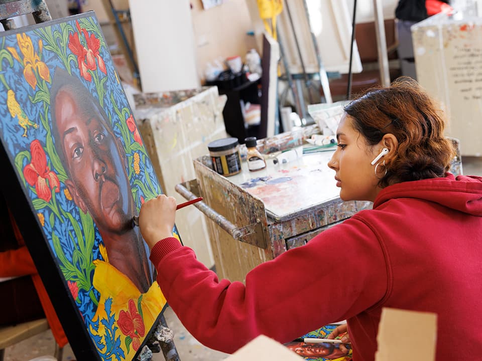 A students focuses on their brushstrokes as they paint a portrait.