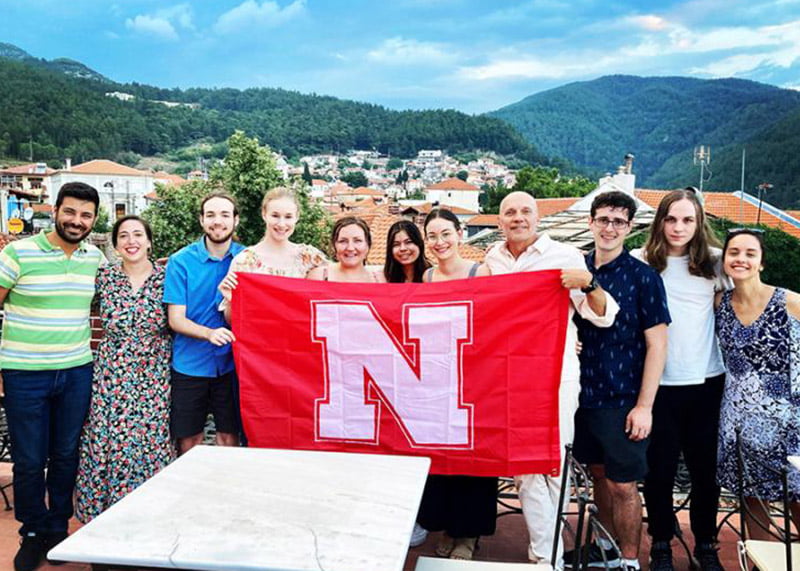 Students and professor hold up UNL flag in Greece.