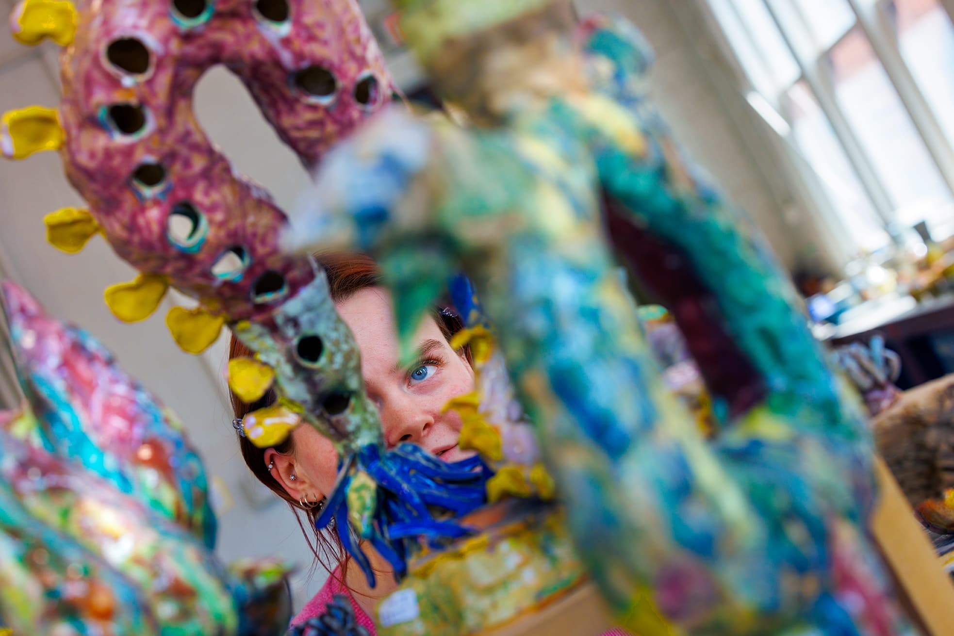 A close up of a students eye looking through a gap in a pottery sculpture.