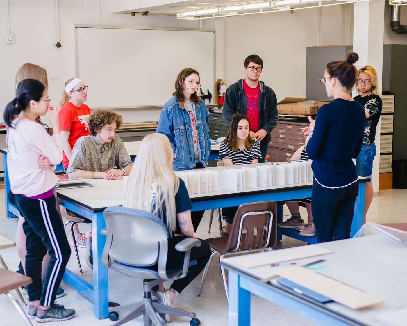 An instructor stands reviewing a project with students all around.