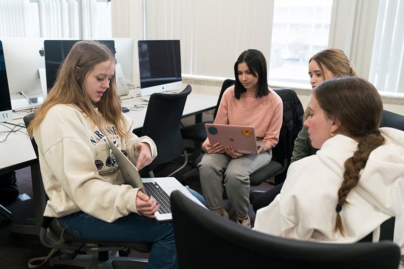 Students in a computer lab look at a laptop monitor.