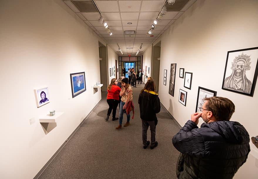 People stand looking at art work hung along walls.