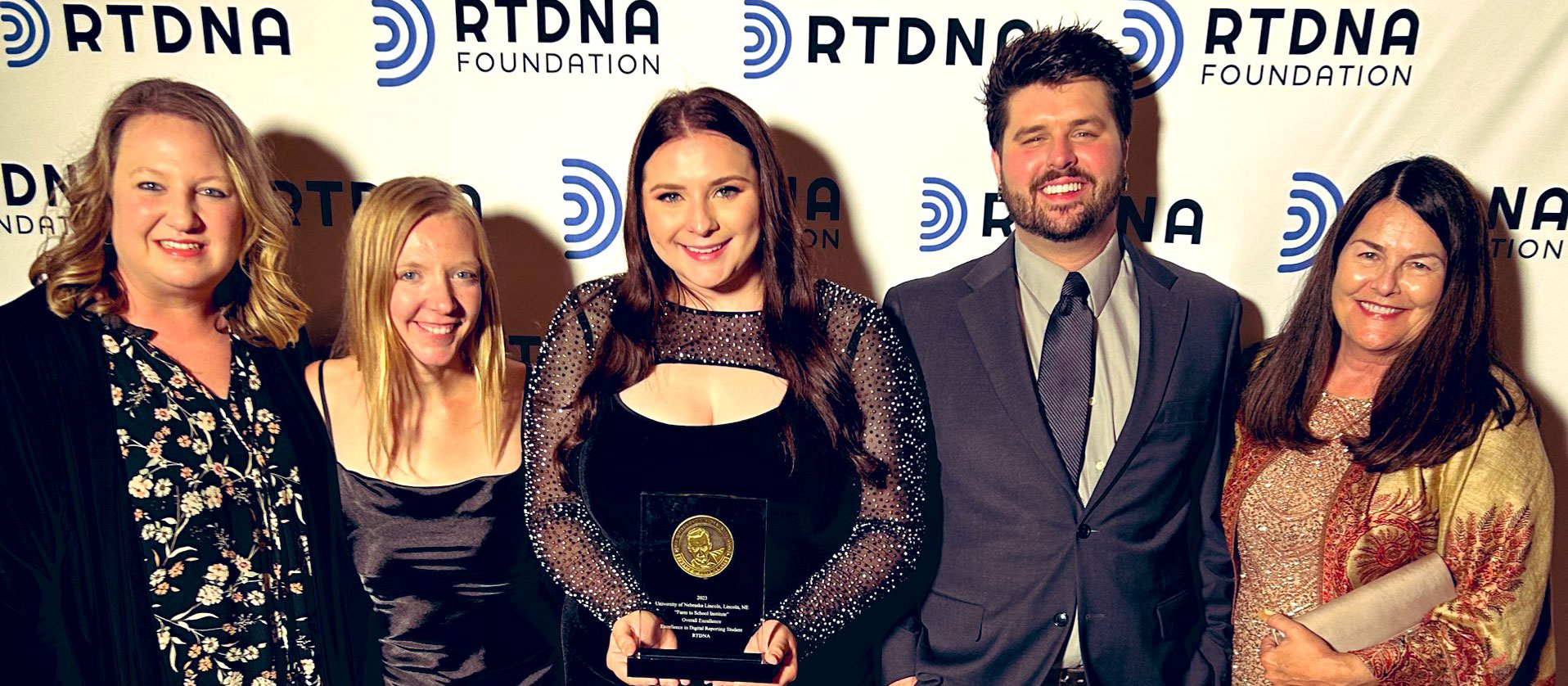 Five people stand with the center person holding an award