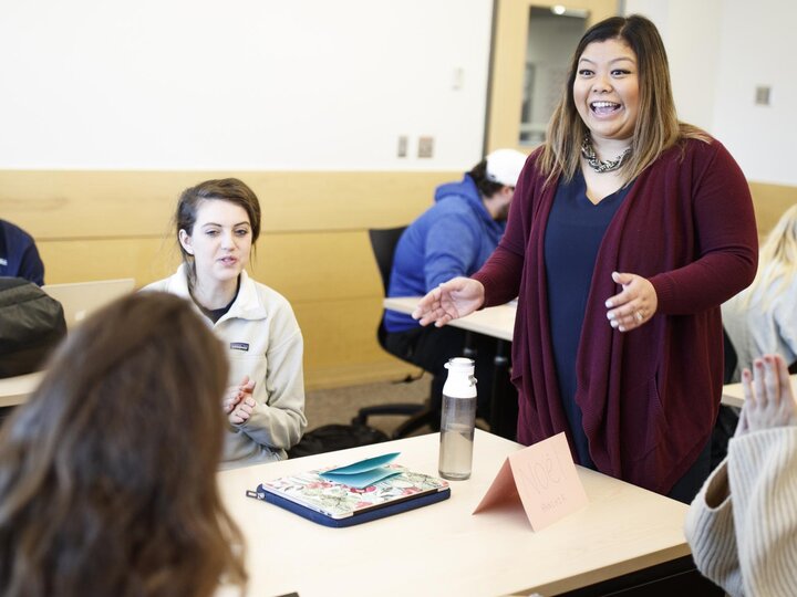 Woman stands next to desk talking to two students