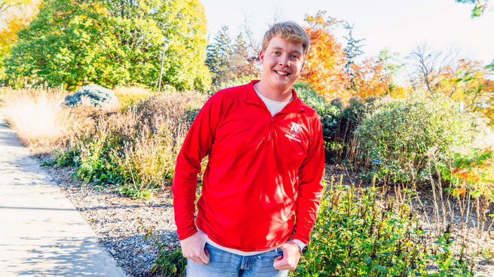 Student wearing red pullover standing next to East Campus arboretum