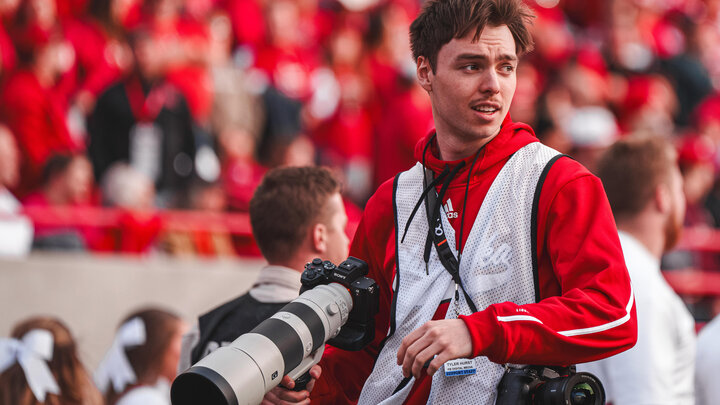 Student wearing reflective vest and holding camera on field at Memorial Stadium
