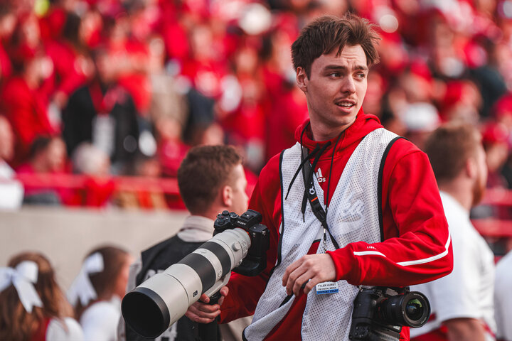 Student wearing reflective vest and holding camera on field at Memorial Stadium
