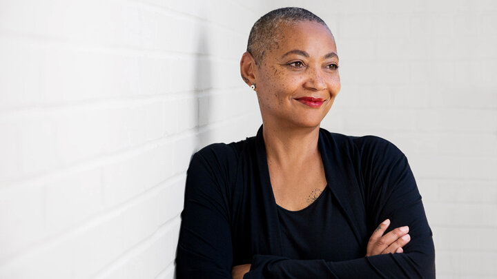 Color portrait of artist Elizabeth Burden, wearing a black shirt and sweater, with her arms crossed.