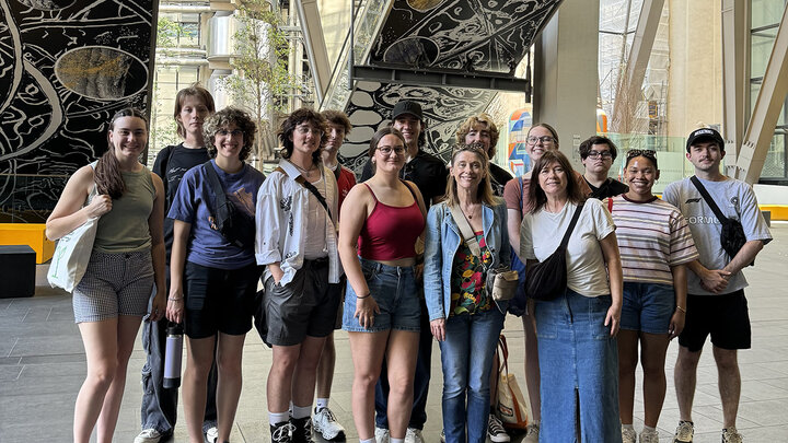 Group of people smiling indoors with artwork and large windows in the background. Emerging media arts students visit Jane and Louise Wilson’s installation titled “Dendrophiles,” which is installed at The Leadenhall in London. Courtesy photo.