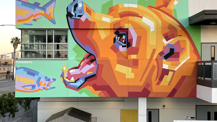 Colorful geometric mural of a bear's head with fish on a building's green wall.