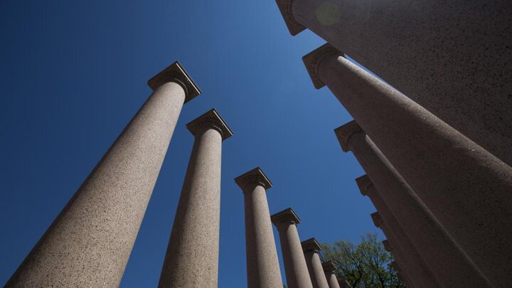 Tall stone columns beneath a clear blue sky, viewed from below.