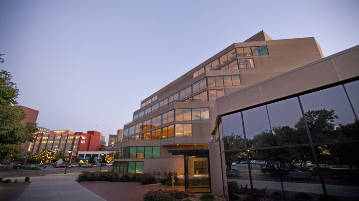 Modern building with large windows, surrounded by brick pathways and trees, under a twilight sky.
