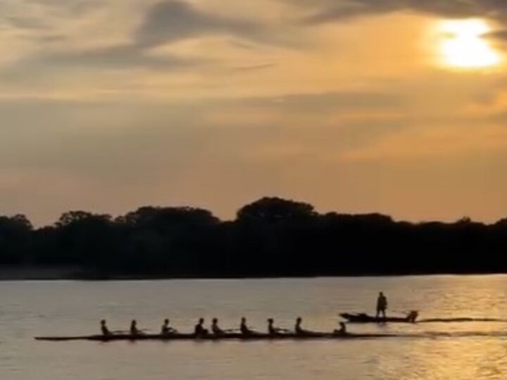A rowing shell of 8 members at sunrise with teh coach launch following.