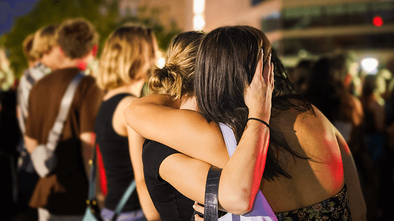 Two women embrace in greeting at night outdoor concert.