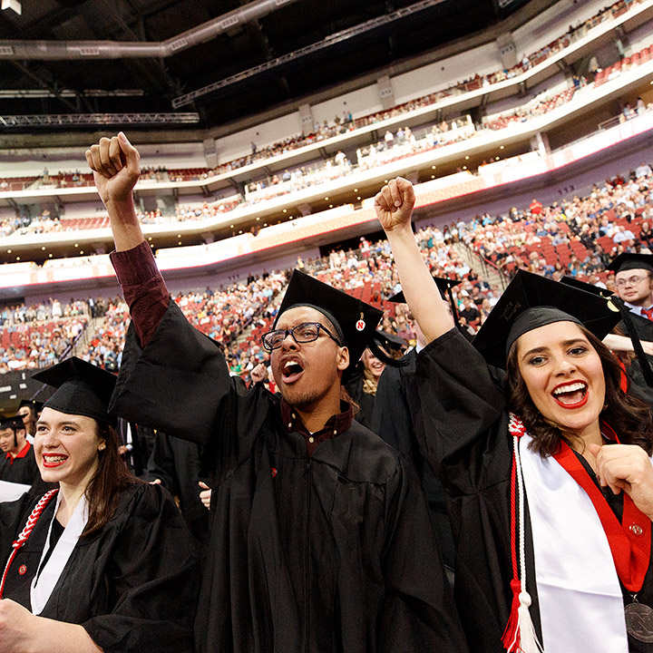 Graduates raise fists and cheer at commencement.