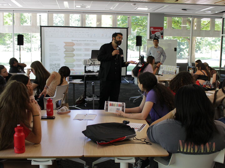 Librarian at front of room with microphone providing instruction to students at tabletops