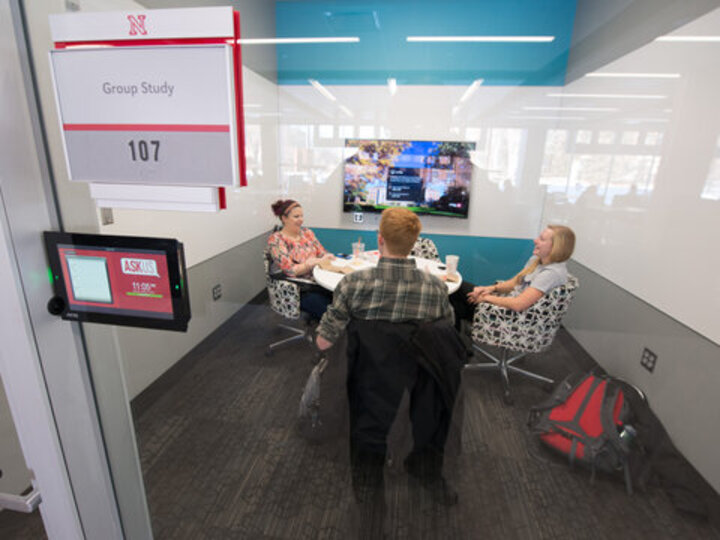 Study room with students around table with a reservation tablet, white boards and technology in the room.